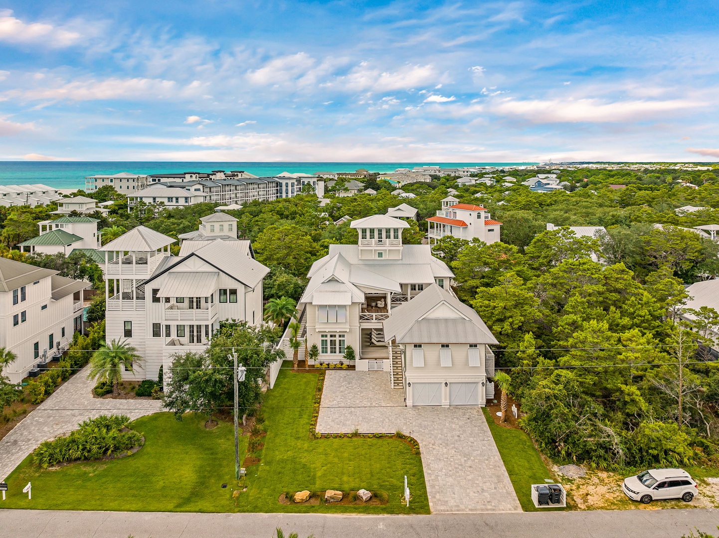 An aerial view captures the property nestled among lush greenery in a coastal neighborhood, with stunning ocean waters visible in the distance.