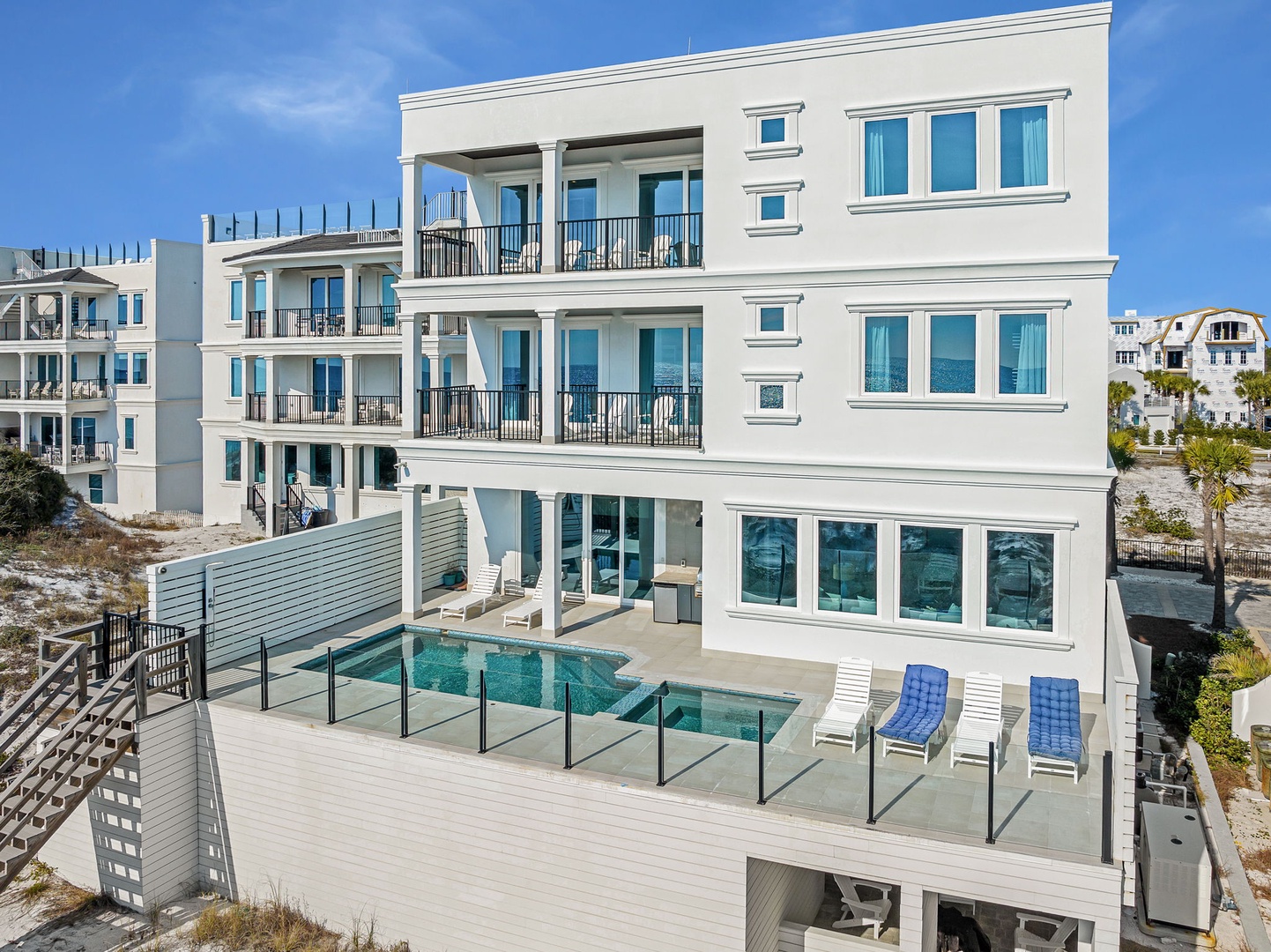 Modern three-story beachfront property featuring multiple balconies, a private pool with safety fencing, and contemporary architecture in a coastal neighborhood.