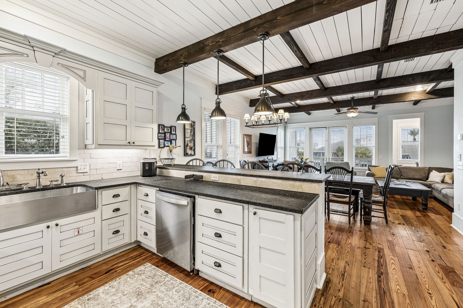 Gather in this open-concept kitchen and dining space where vaulted ceilings with rustic beams meet coastal charm. A chef's island invites conversation as sunlight streams through plantation shutters.