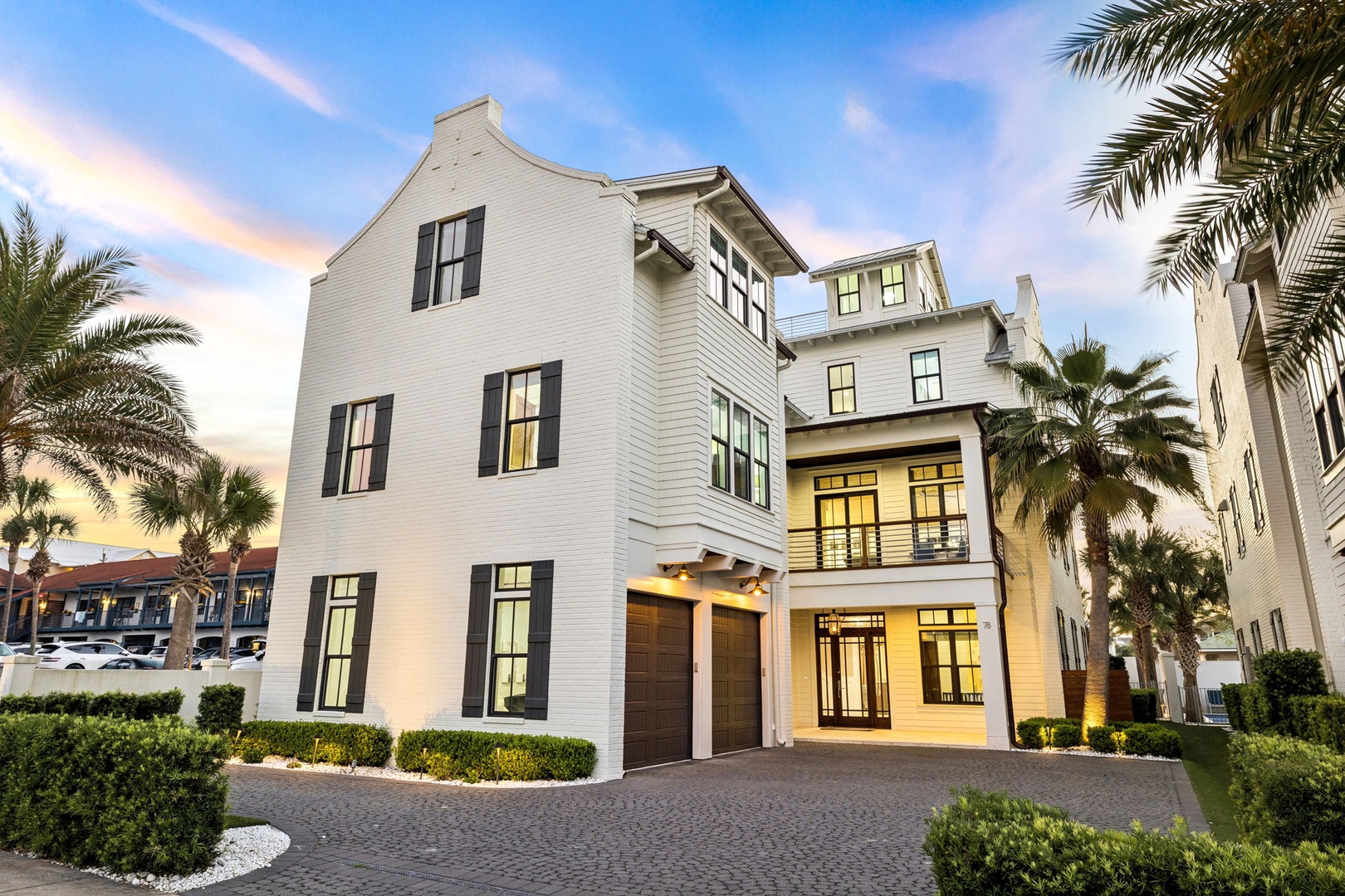 Elegant coastal architecture features pristine white siding and tropical palms under a painted evening sky.