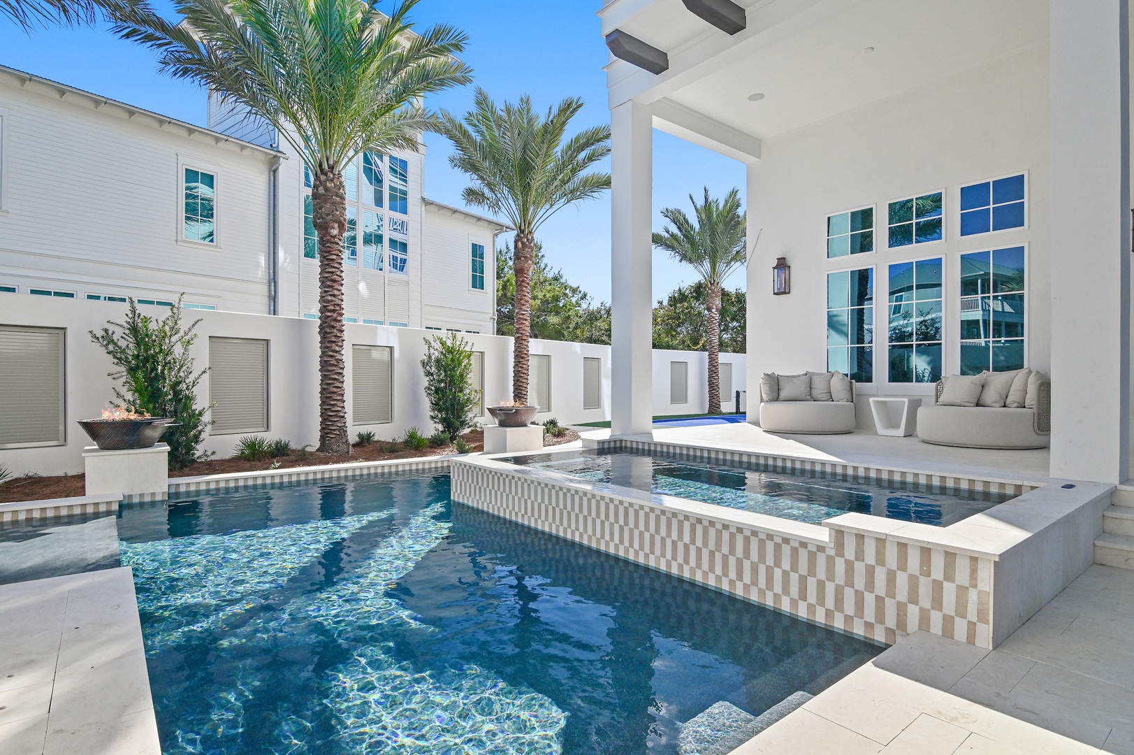 Modern luxury property featuring a private pool surrounded by tropical palms and elegant white architecture under clear blue skies.
