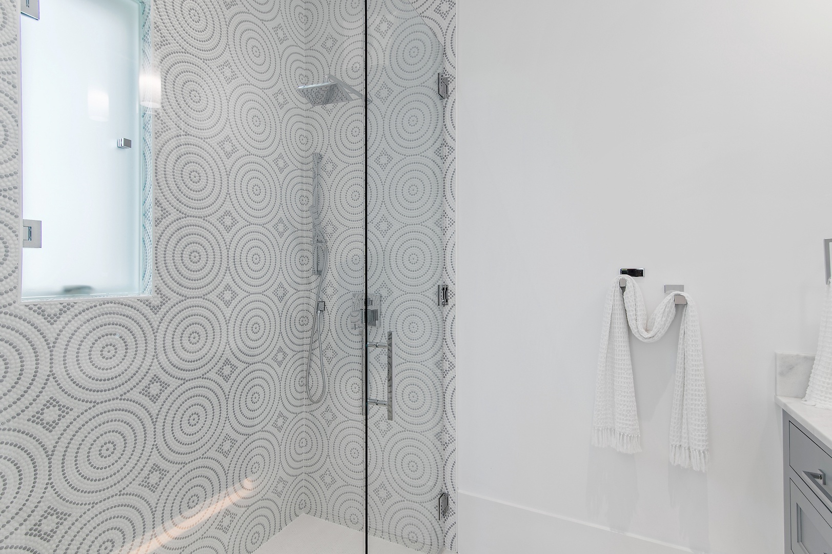 Step into your sleek, spa-like bathroom featuring a stunning glass-enclosed shower with artistic circular mosaic tiles. Fresh towels await you in this bright, modern space.