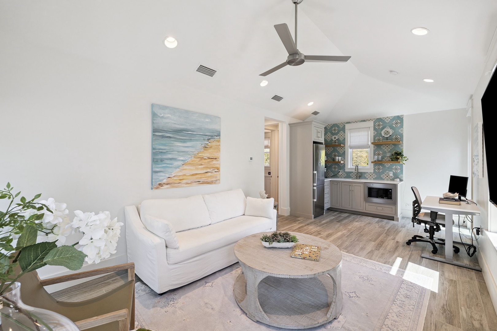 Step into your bright, modern living space featuring coastal artwork, comfortable seating, and an open kitchen with stylish tile backsplash.