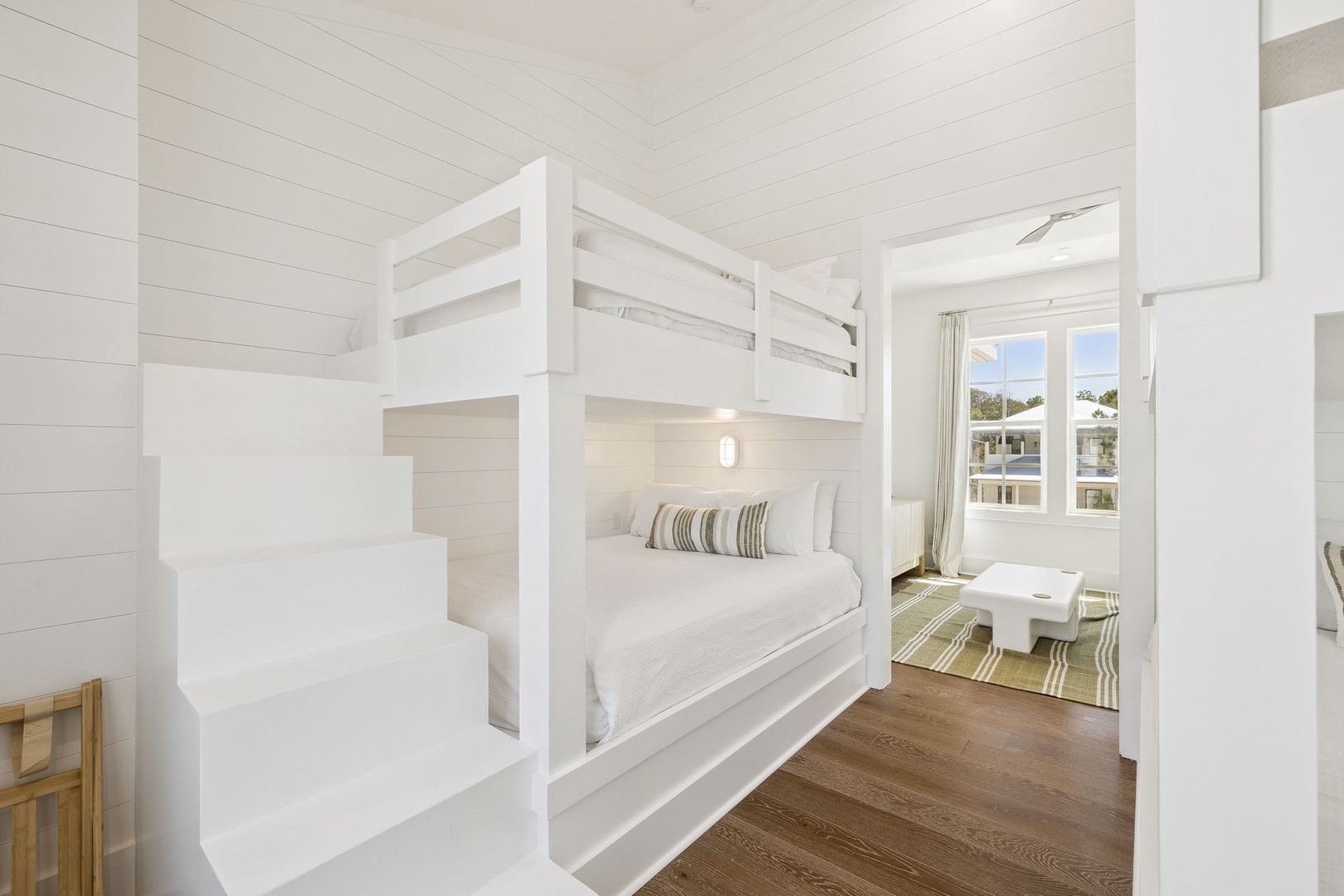 Your coastal retreat features charming bunk beds perfect for families, with crisp white linens and warm wood floors creating a serene seaside atmosphere.