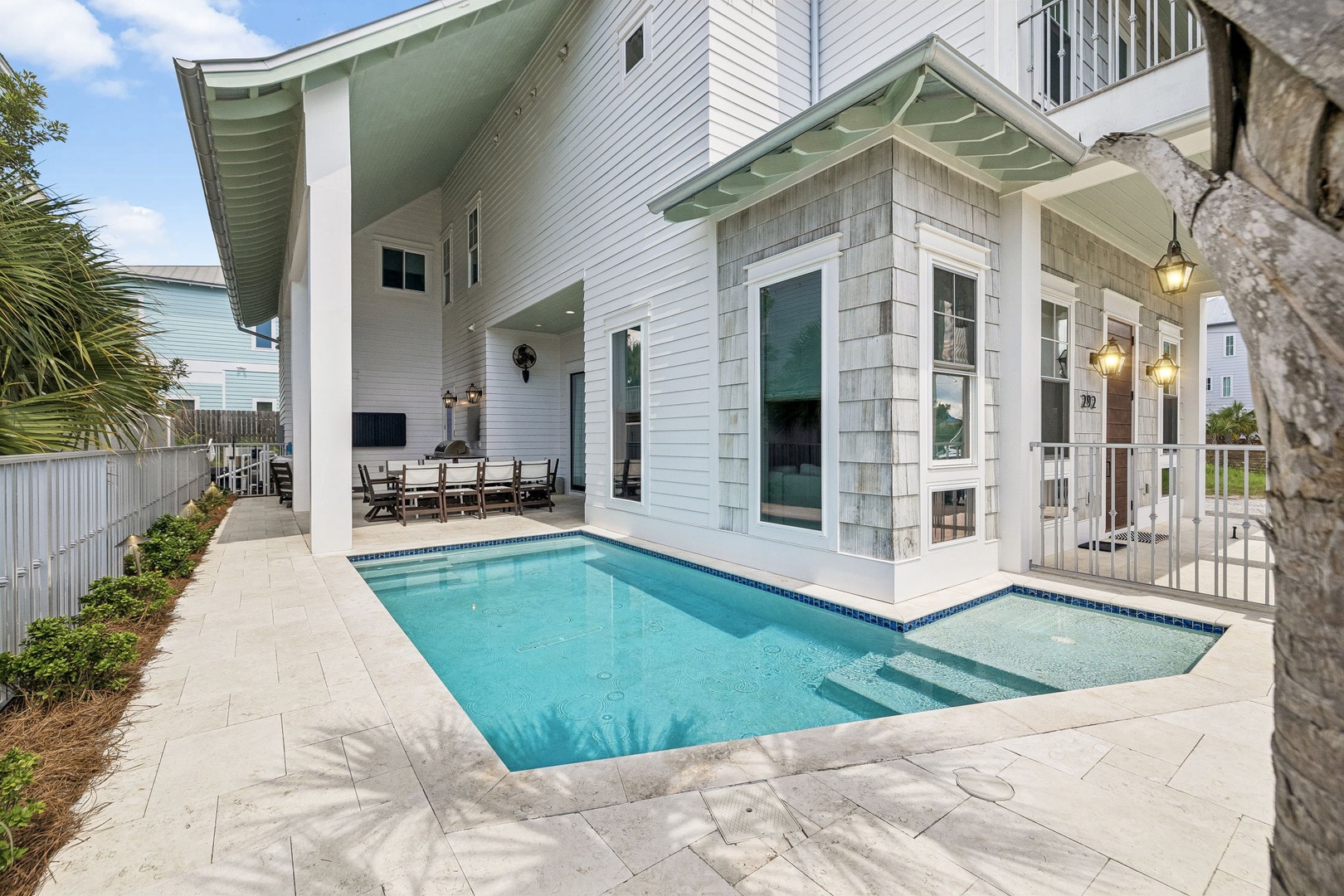 This beautiful coastal-style property features modern architecture with light-toned siding and spacious covered porches, located in a peaceful neighborhood with palm trees and clear skies.