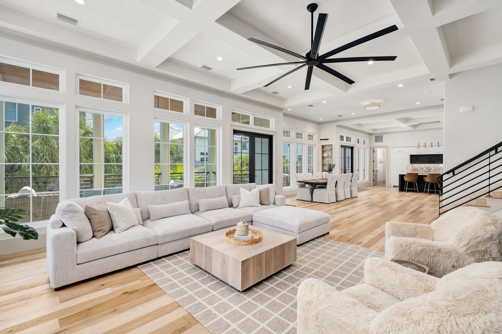 Relax in your luxurious open-plan living space with soaring coffered ceilings, plush seating, and floor-to-ceiling windows flooding the room with natural light.