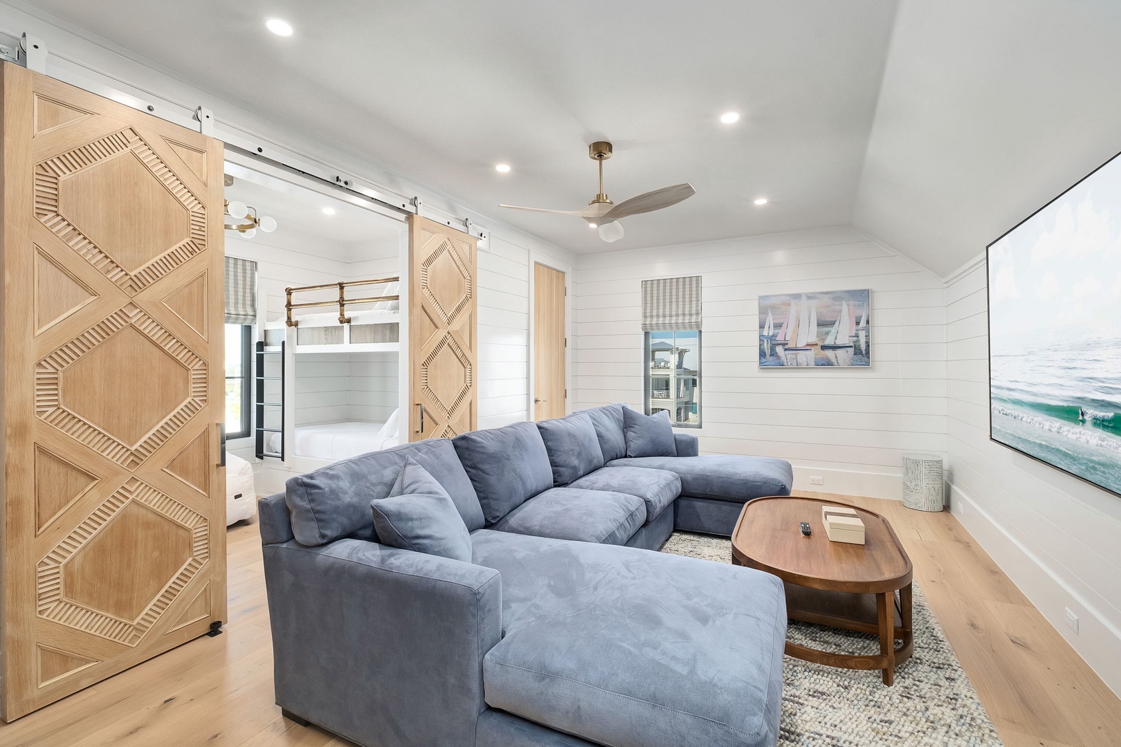 Sink into plush sectional seating while coastal artwork and sliding barn doors create your perfect retreat for relaxation and entertainment.