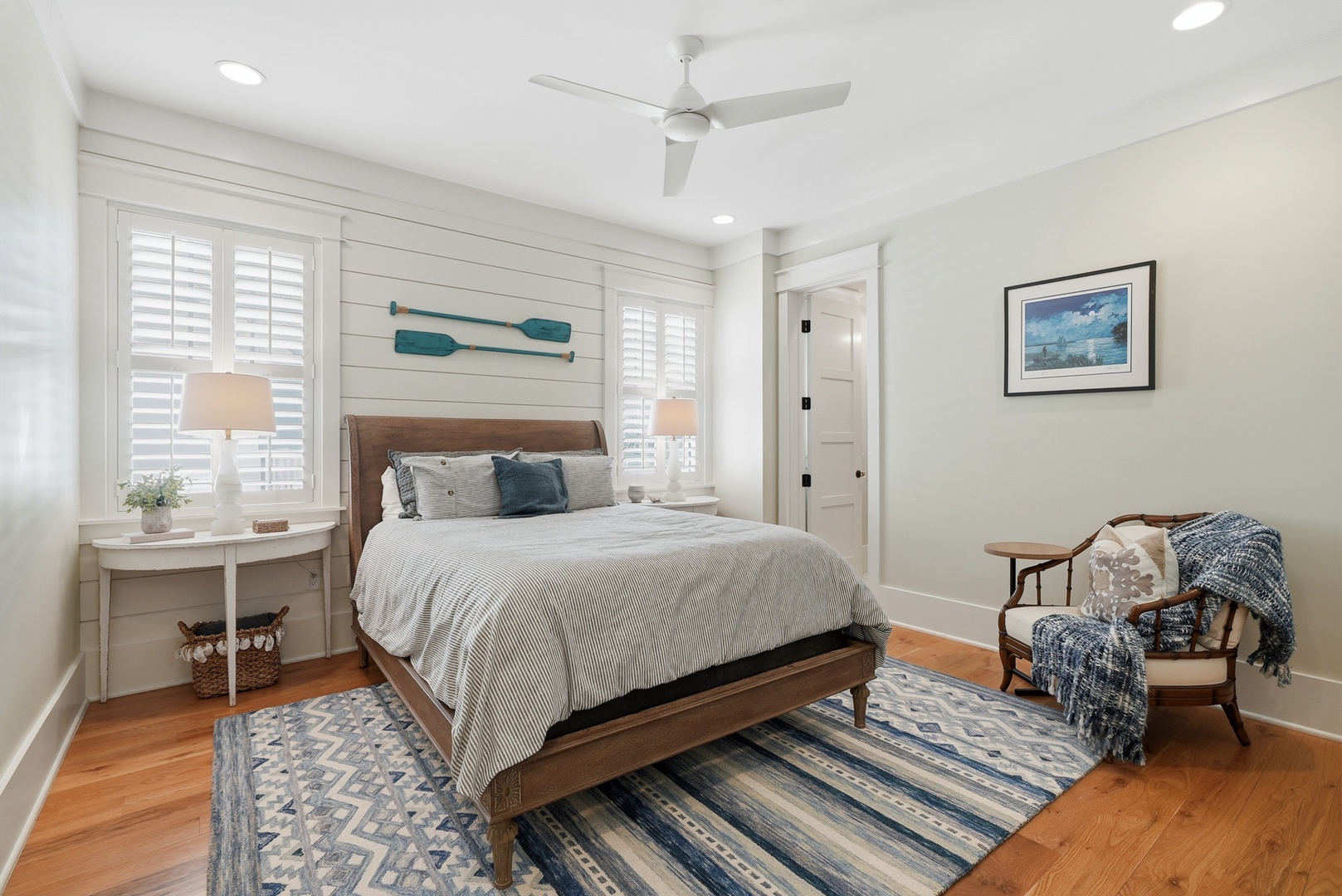 Unwind in your serene coastal bedroom with crisp linens, ceiling fan, and charming nautical touches. Soft natural light and a cozy reading chair invite peaceful mornings and restful nights.