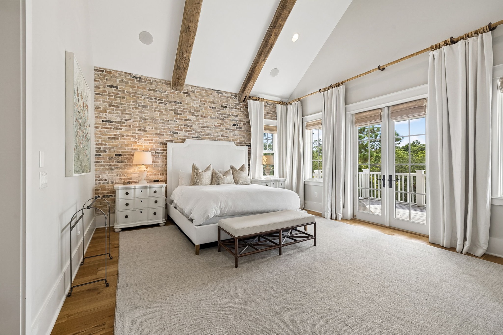 Sink into your private retreat where rustic beams meet modern elegance, crisp linens await, and French doors frame serene greenery—your perfect escape from the everyday.