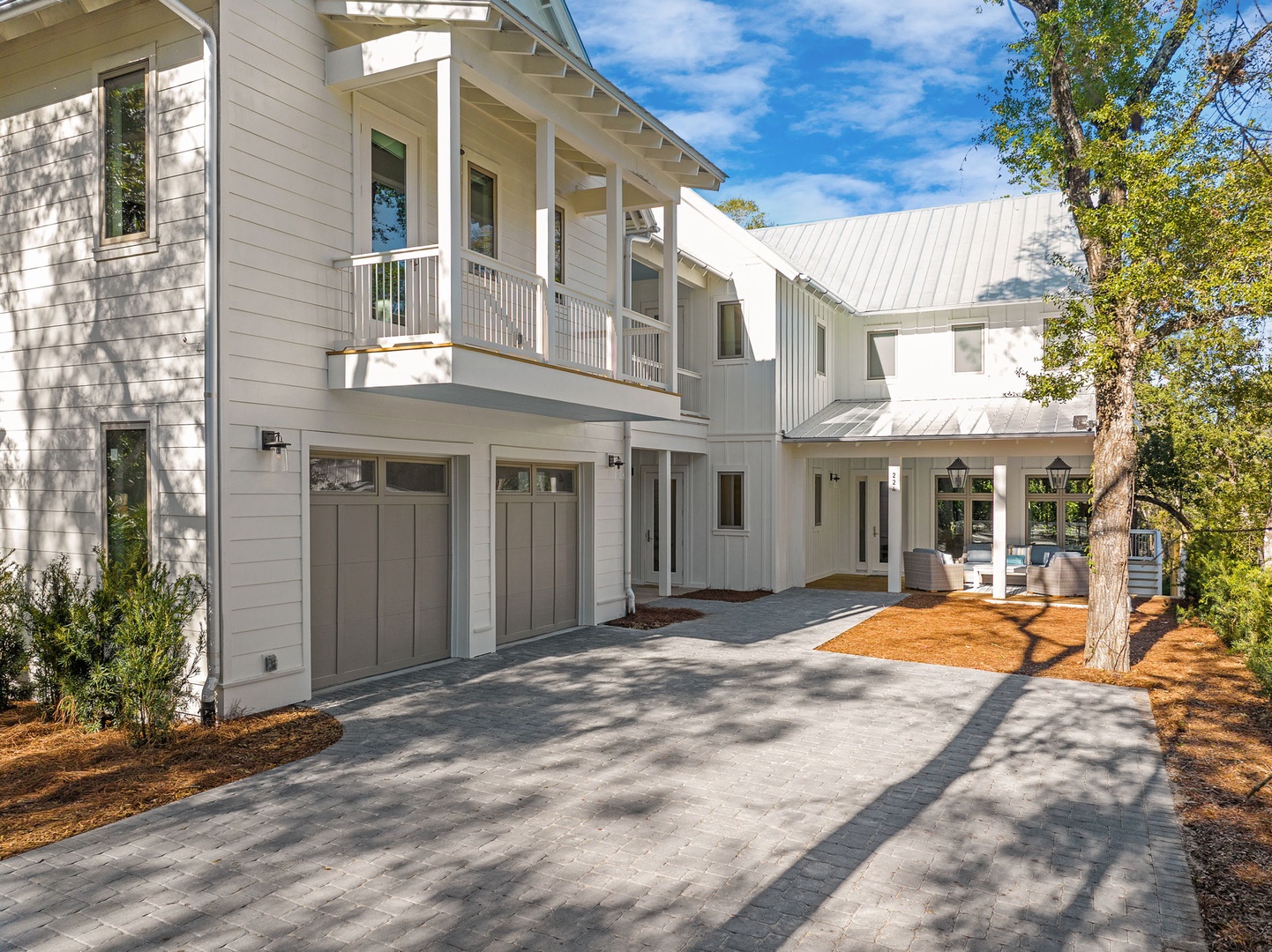 Modern coastal-style home with spacious driveway and garage, surrounded by mature trees in a peaceful neighborhood setting.
