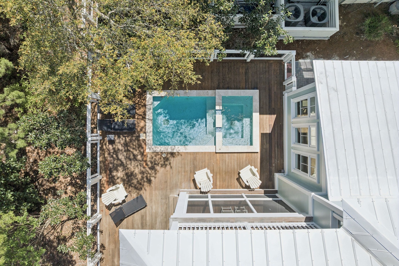 Aerial view of property showing swimming pool, deck area, and surrounding wooded landscape.