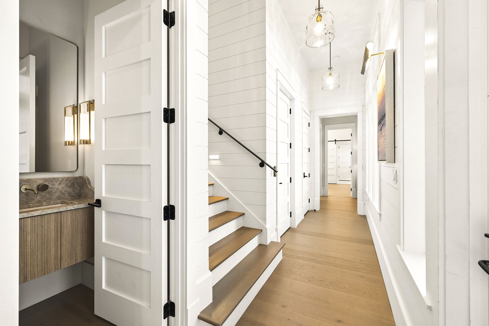 A bright hallway with stylish details—notice the modern lighting, warm wood floors, and the inviting stairway that carries you between floors. Clean lines and thoughtful touches make every step feel welcome.