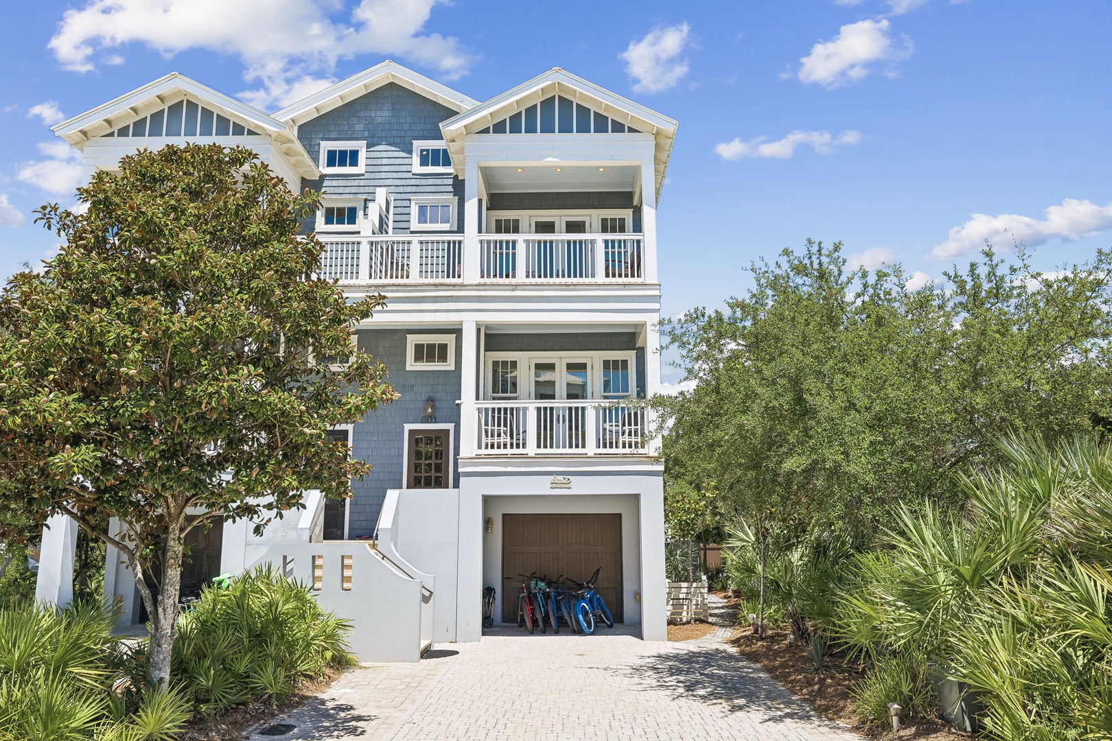 A charming coastal property surrounded by lush tropical landscaping and sheltered trees. The home features white-trimmed balconies and sits in a peaceful residential area near the beach.