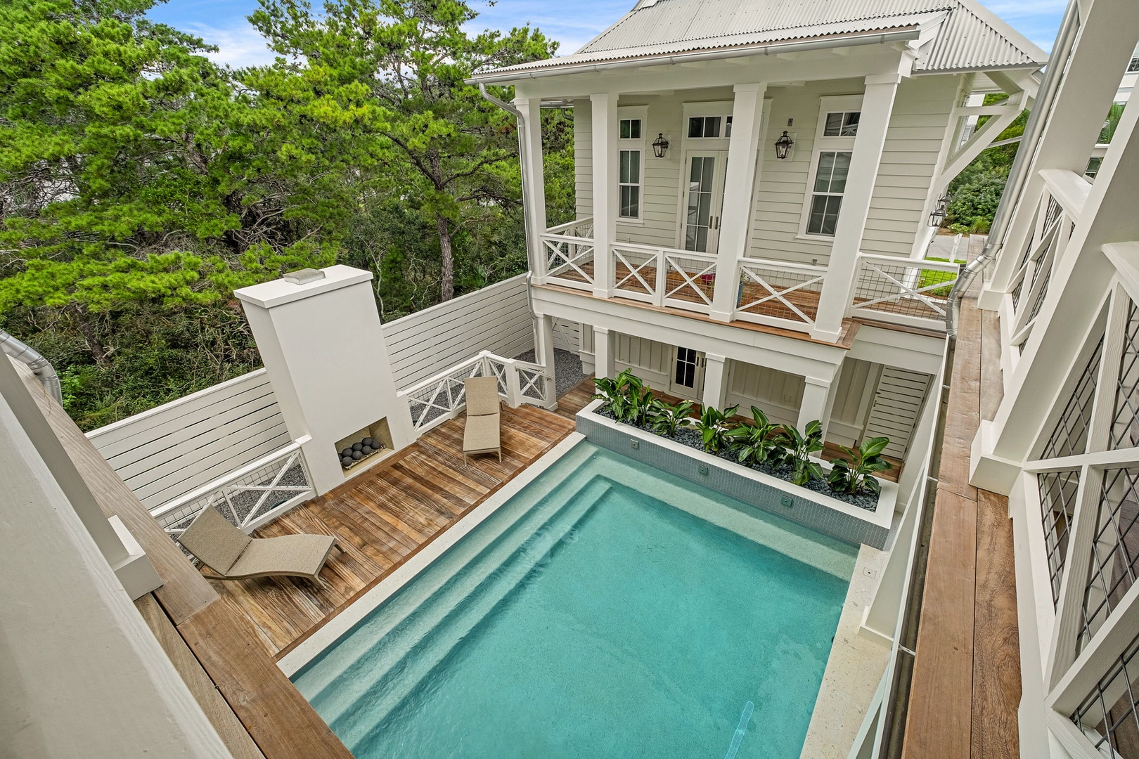 An elegant private courtyard features a sparkling pool surrounded by rich wooden decking, inviting you to unwind in your own tranquil oasis framed by lush tropical greenery and classic white balconies.