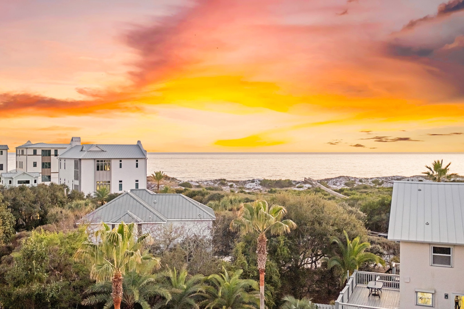 Spectacular sunset paints the sky in golden hues over this coastal community, with palm trees and beach homes creating a perfect tropical setting.
