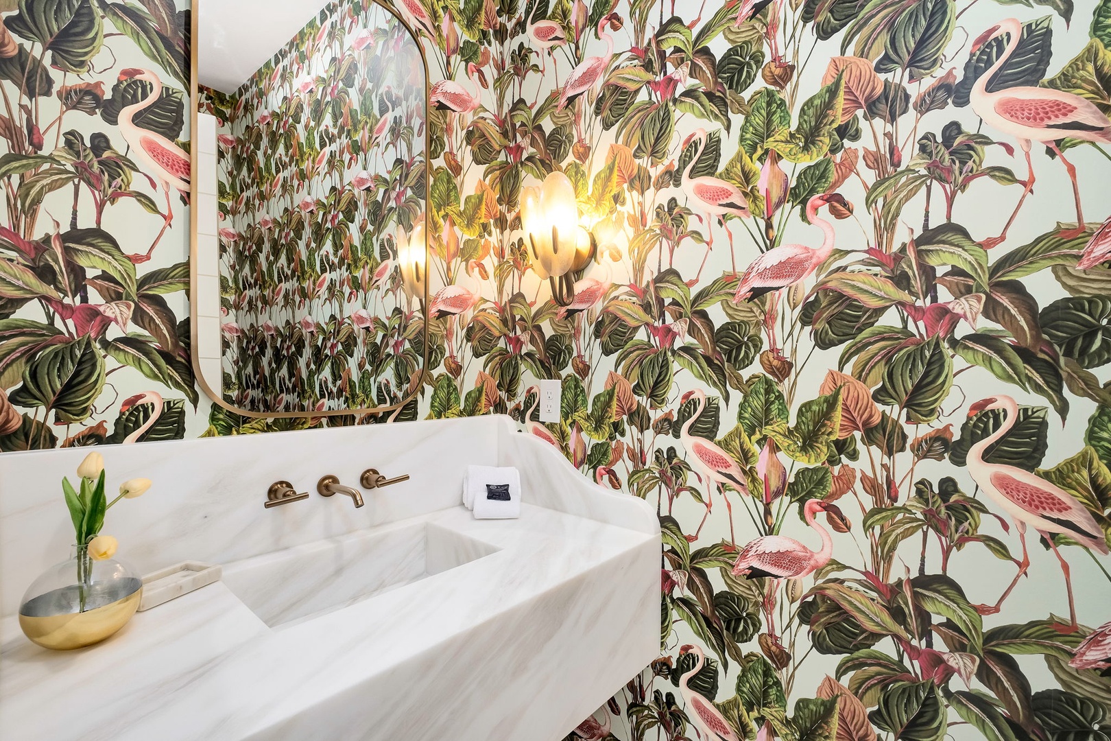Step into a bathroom where vibrant tropical wallpaper transforms your daily routine into an escape. The elegant marble vanity and warm lighting create a sophisticated yet playful atmosphere you'll love.