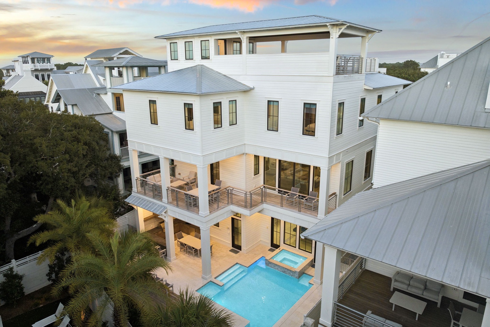 Stunning multi-level coastal home featuring a sparkling pool and spacious covered porches, nestled among palm trees in an upscale neighborhood.