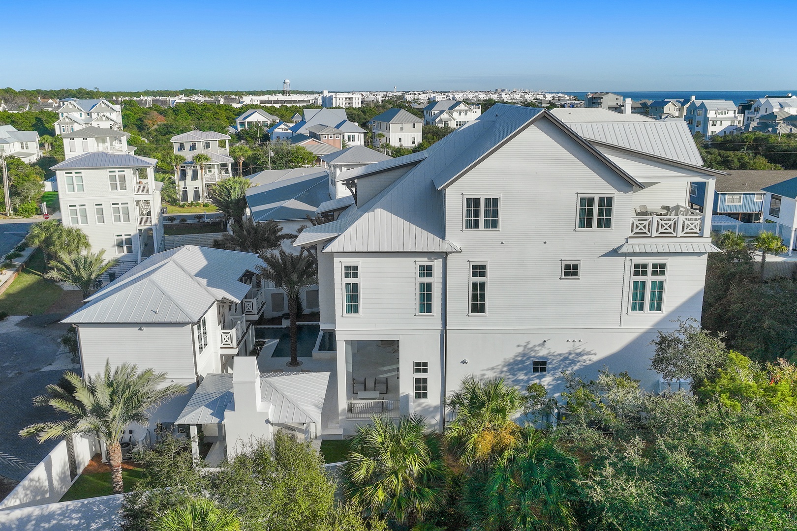 Aerial view of a coastal vacation home in a scenic beachside neighborhood, surrounded by lush greenery and just moments from the ocean.