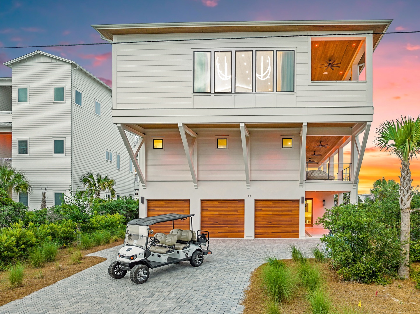 Modern coastal property featuring contemporary architecture, tropical landscaping, and convenient parking beneath covered carport areas at sunset.