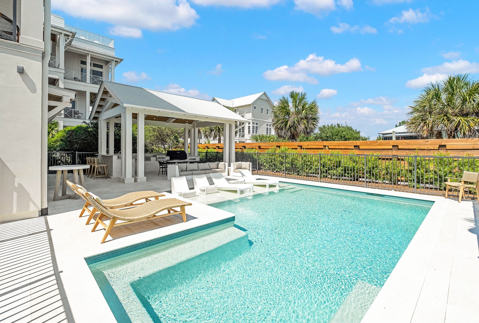 A coastal retreat featuring a private pool with tanning ledge, covered pavilion, and tropical palms framing a peaceful neighborhood setting under bright blue skies.