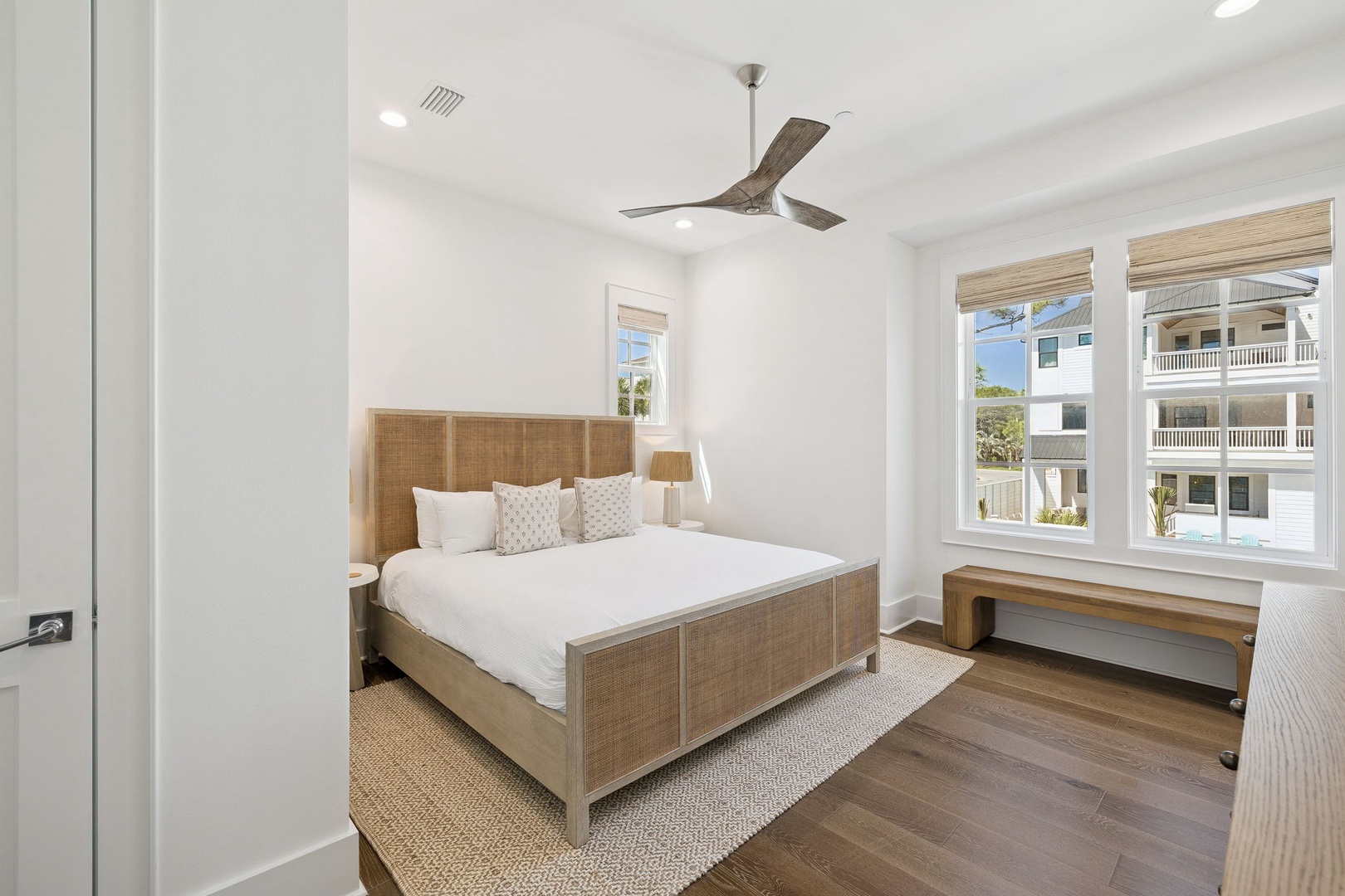 Unwind in your serene bedroom featuring a cozy wicker-framed bed, soft linens, and bright windows that fill the space with natural light.