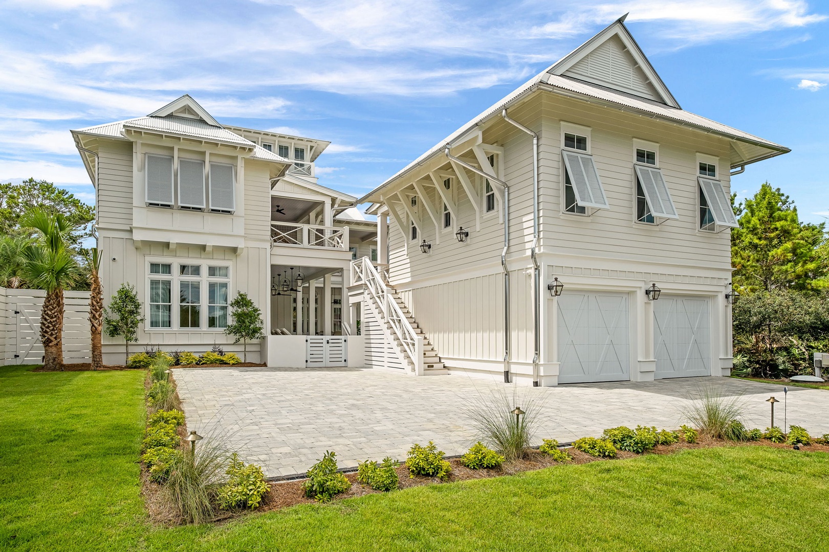 A coastal-style property with elegant white siding, spacious garage, and landscaped grounds set beneath a bright blue sky.