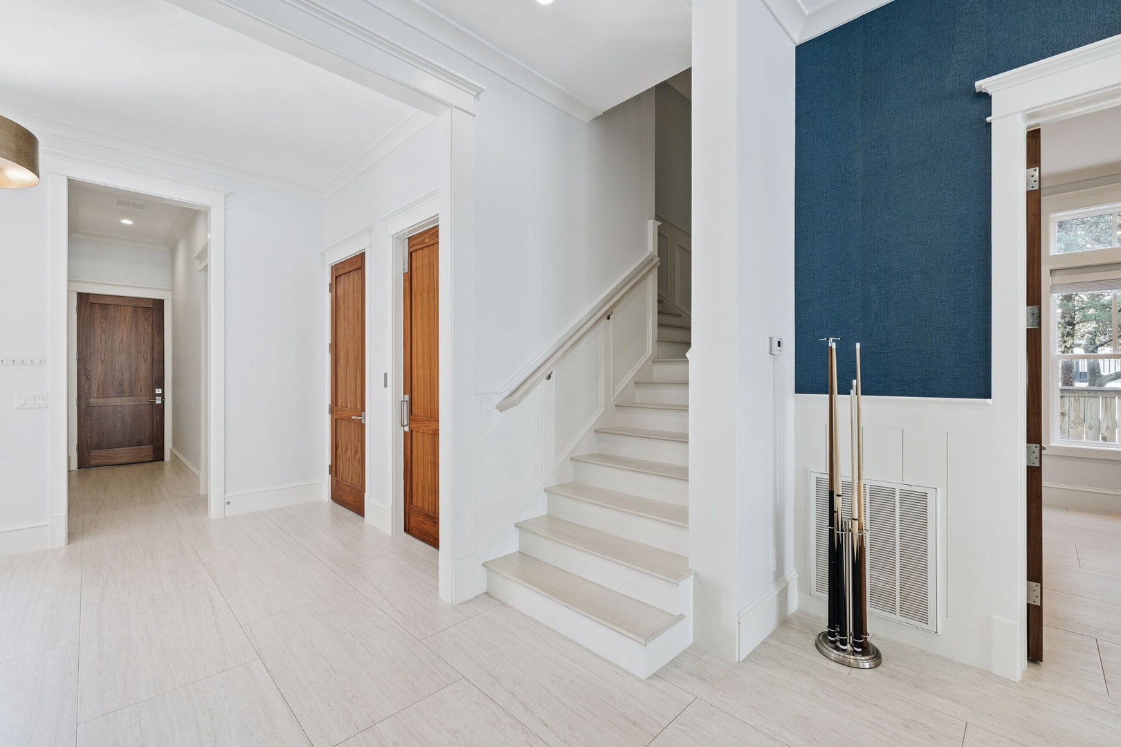 Step into your elegant entryway featuring pristine white stairs, rich navy accent wall, and warm wood doors that welcome you home.