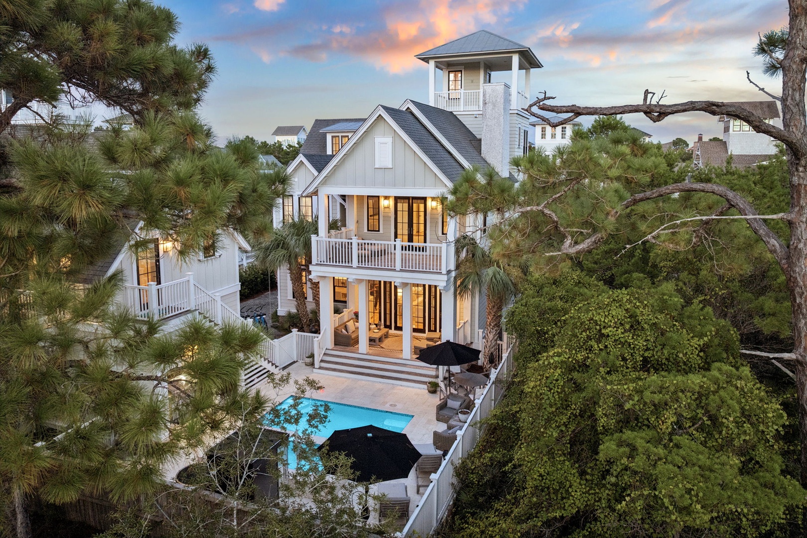 A striking coastal home featuring elegant architecture, a private pool, and a charming observation tower nestled among lush greenery, captured during the golden hour.