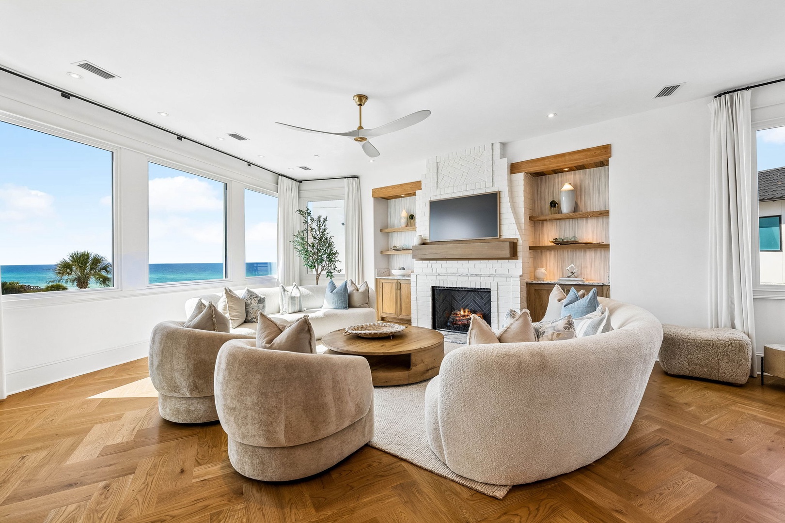 Unwind in this serene living room where coastal breezes meet elegant comfort. Sink into plush seating as sunlight dances across warm wood floors, while panoramic windows frame endless ocean views that bring the beach to you.