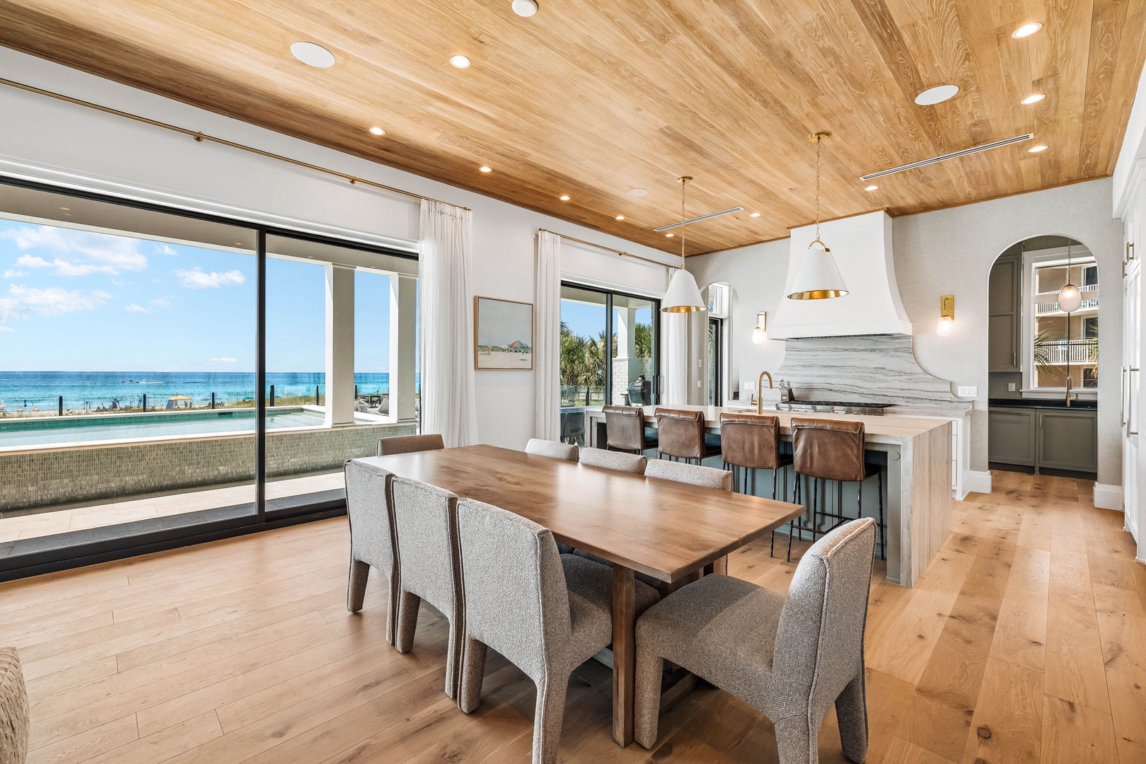 Step into your dream coastal retreat where rich wood ceilings meet stunning ocean views. Gather around the spacious dining table with loved ones while soaking in endless turquoise waters just beyond the glass.