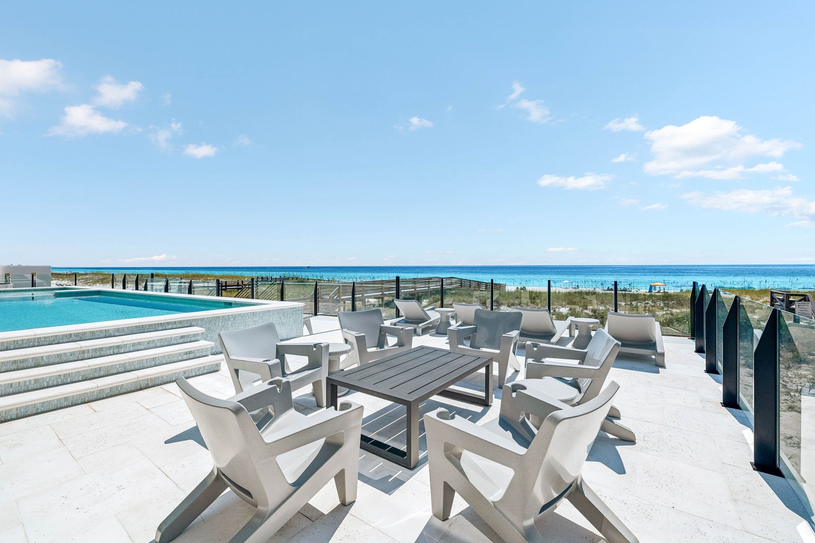 An inviting outdoor terrace area featuring a swimming pool and comfortable seating overlooking a beautiful stretch of sandy beach and turquoise waters—your perfect spot to unwind.