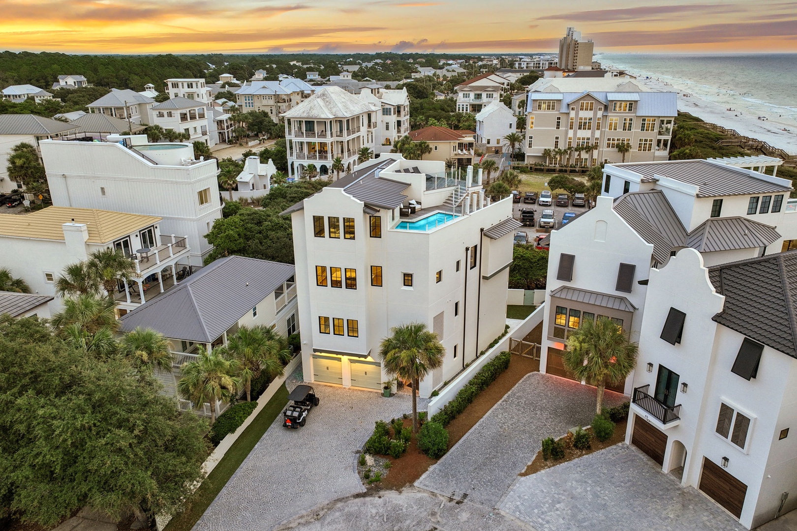 Aerial view of a coastal residential community featuring white architecture, beachfront homes, and stunning sunset over the Gulf. The property is located in a walkable neighborhood near the shore.