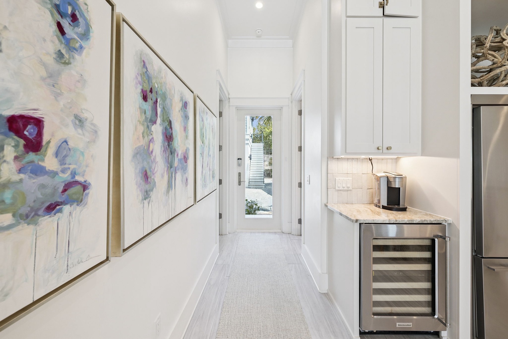 Step into your bright, art-filled hallway where colorful paintings and sleek white cabinetry create an elegant welcome to your home.