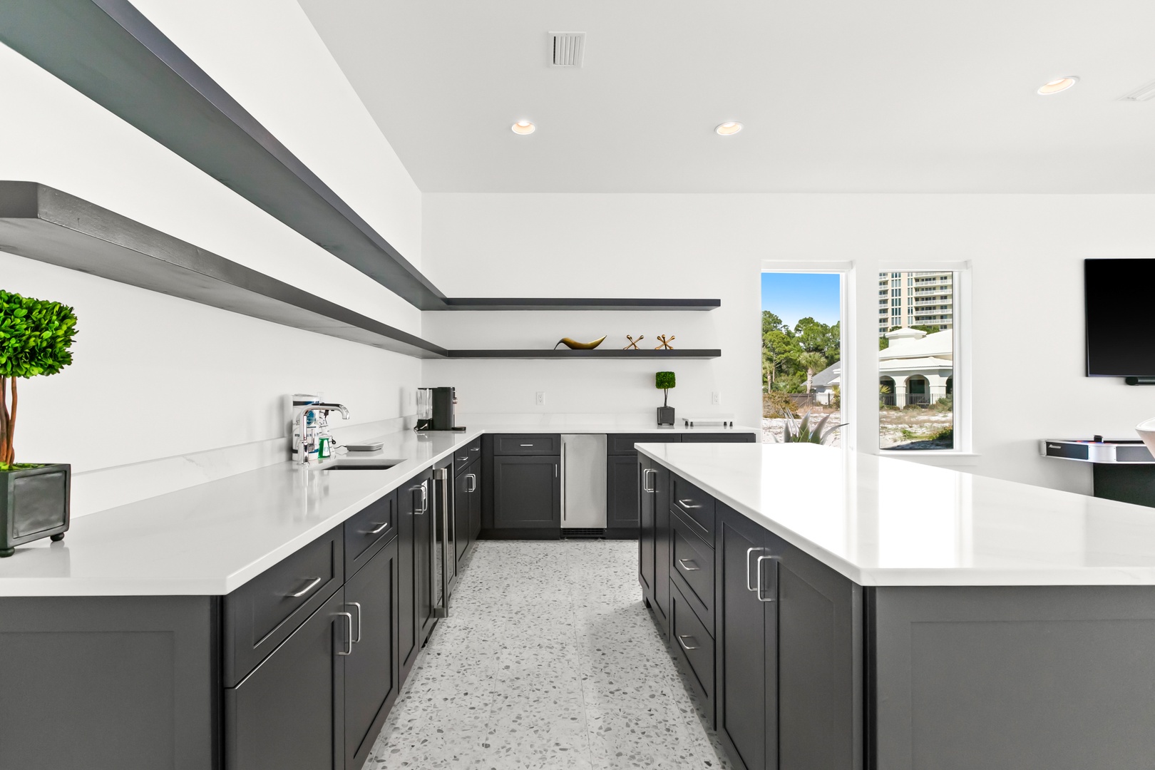 Your sleek modern kitchen features pristine quartz countertops, dark charcoal cabinetry, and stainless steel appliances. Sunlight filters through windows overlooking peaceful natural surroundings, creating an ideal space for meal prep.