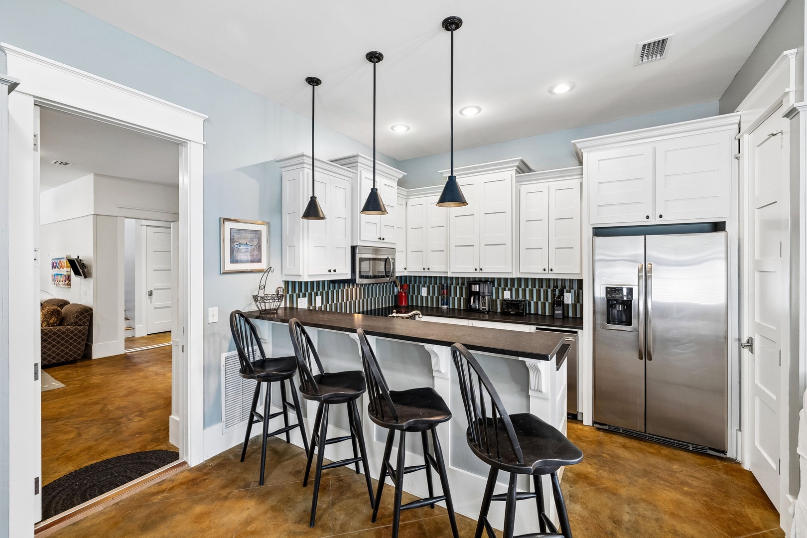 Gather around the breakfast bar in your bright kitchen, where white cabinetry, modern appliances, and sleek pendant lighting create the perfect spot to enjoy morning coffee or casual meals together.