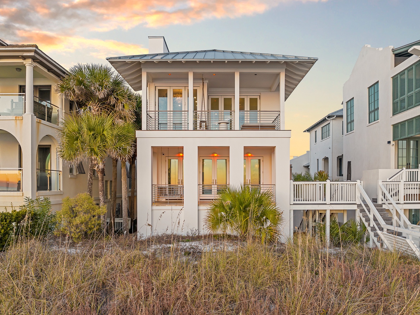 Modern beachfront architecture nestled among coastal palms, with neighboring properties creating a charming seaside community setting.