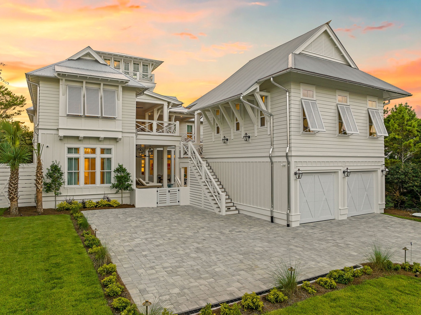 An impressive coastal-style property captured at sunset, featuring two-story architecture with covered balconies, ample parking, and manicured landscaping set against a stunning evening sky.