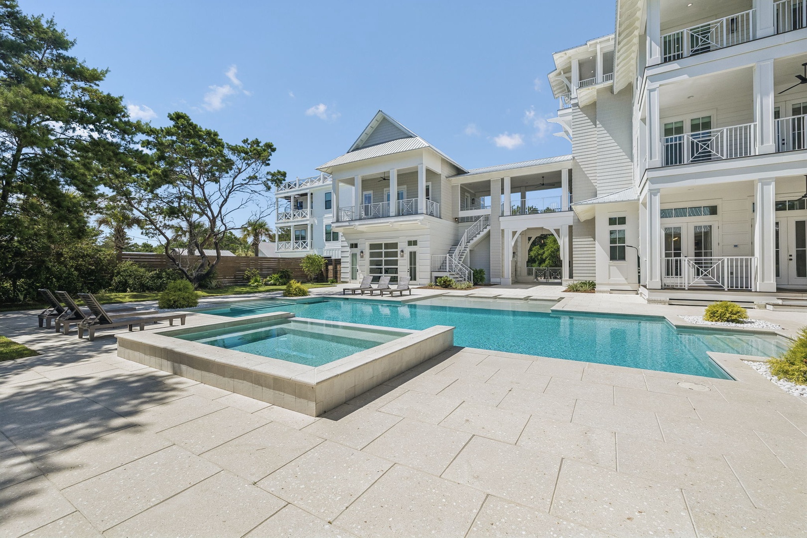 A pristine white coastal estate showcasing a sparkling pool and hot tub surrounded by elegant architecture and lush greenery—this is where your unforgettable vacation begins.