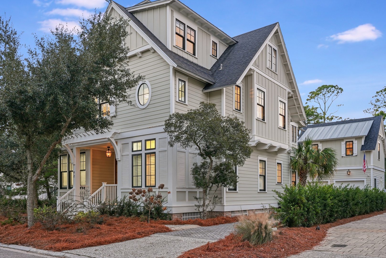 A spacious coastal-style home with classic architectural details, mature landscaping, and warm lighting that welcomes guests at twilight.