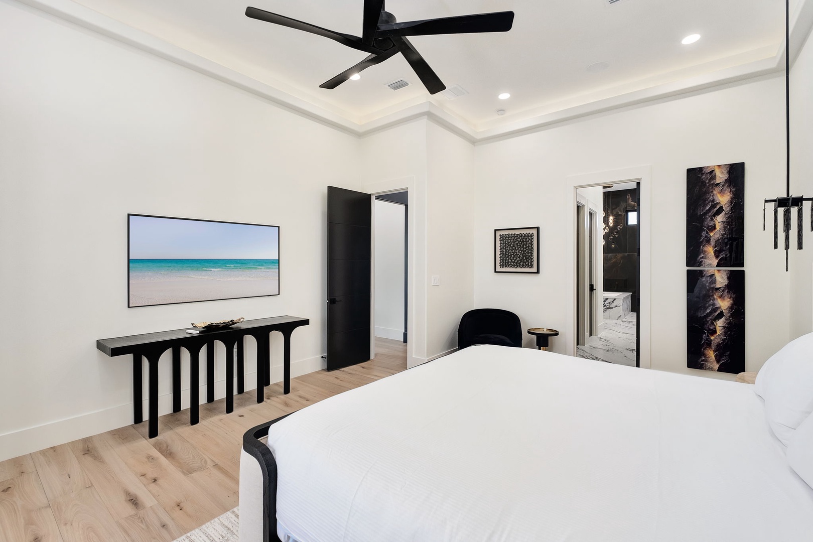 Unwind in your sophisticated bedroom sanctuary featuring crisp white linens, contemporary art, and ocean-view TV for ultimate relaxation.