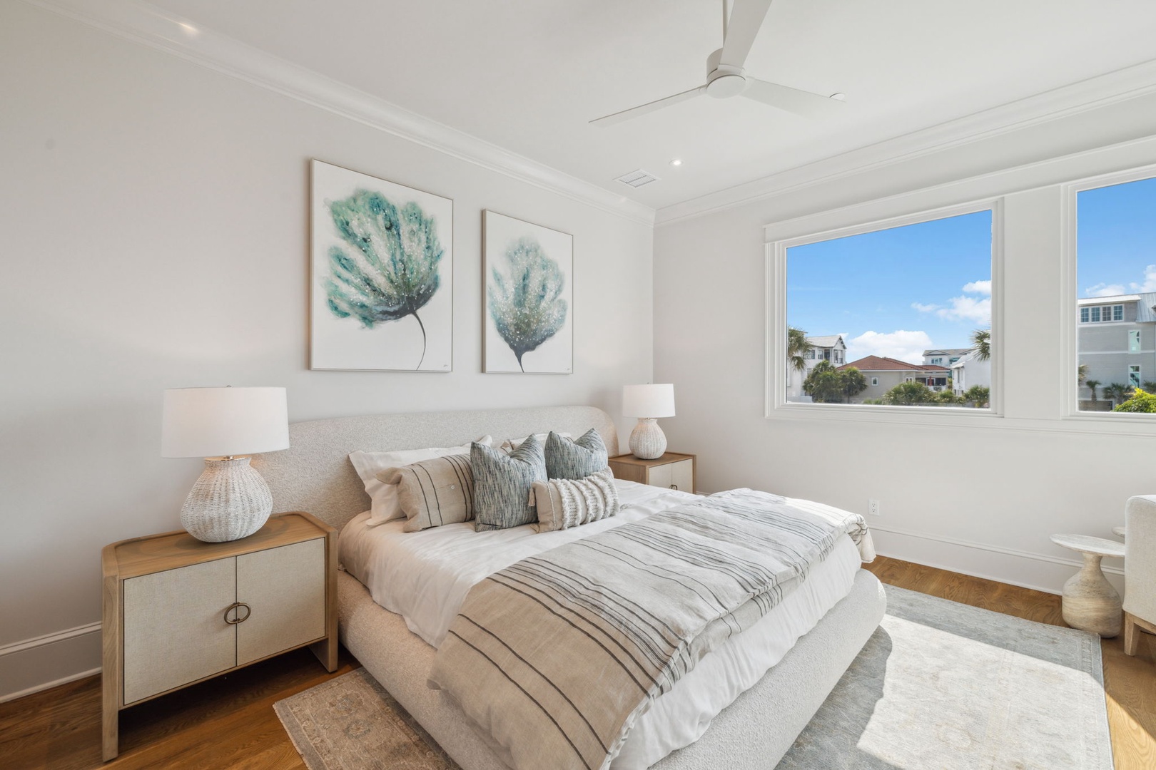 Sink into the plush bedding and wake to sunny neighborhood views framed by bright windows. Coastal-inspired art and a gentle ceiling fan create your serene retreat.