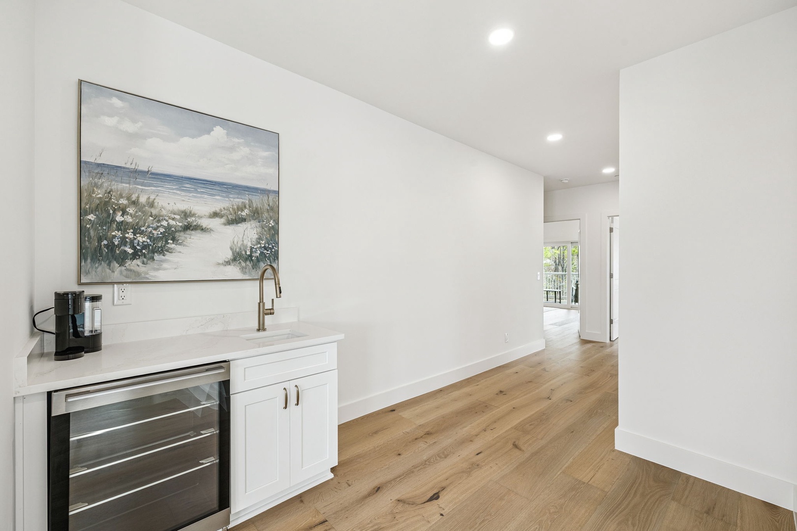 Your stylish wet bar awaits with elegant white cabinetry, wine fridge, and coastal artwork creating the perfect entertaining space.
