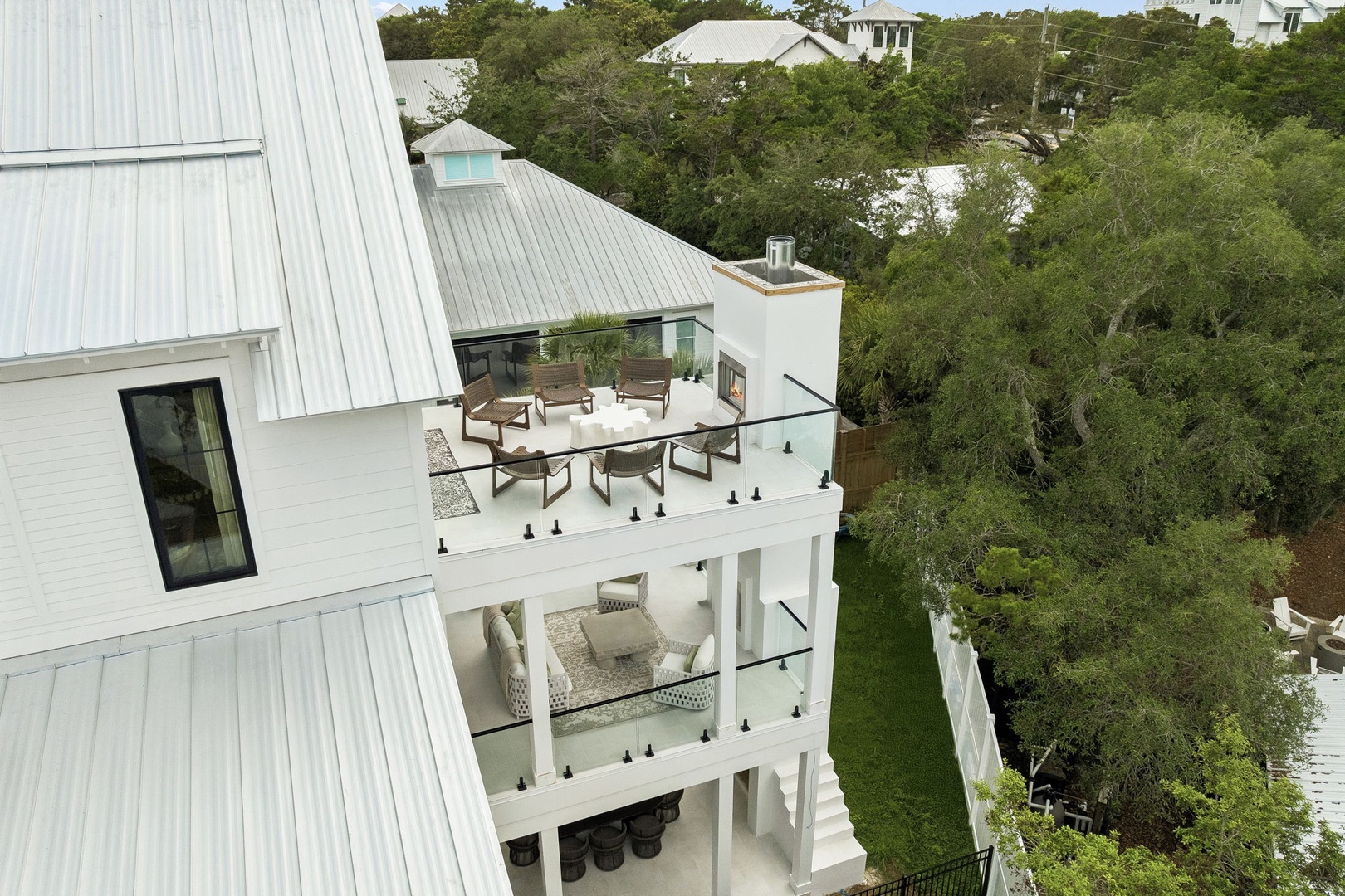 Aerial view of a modern coastal rental with tiered balconies, outdoor seating, and lush tree canopy surroundings in a quiet residential area.