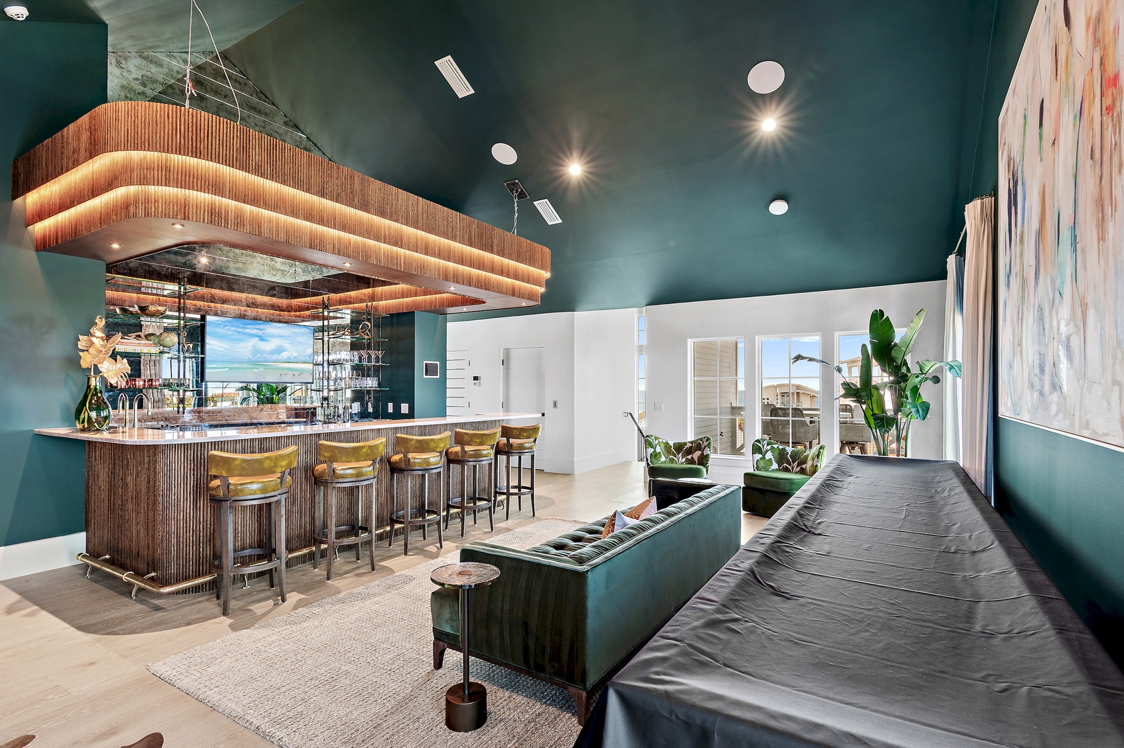 Unwind in this stunning lounge area with rich teal walls, a striking wood-slatted bar, and a cozy seating nook bathed in natural light from the terrace beyond.