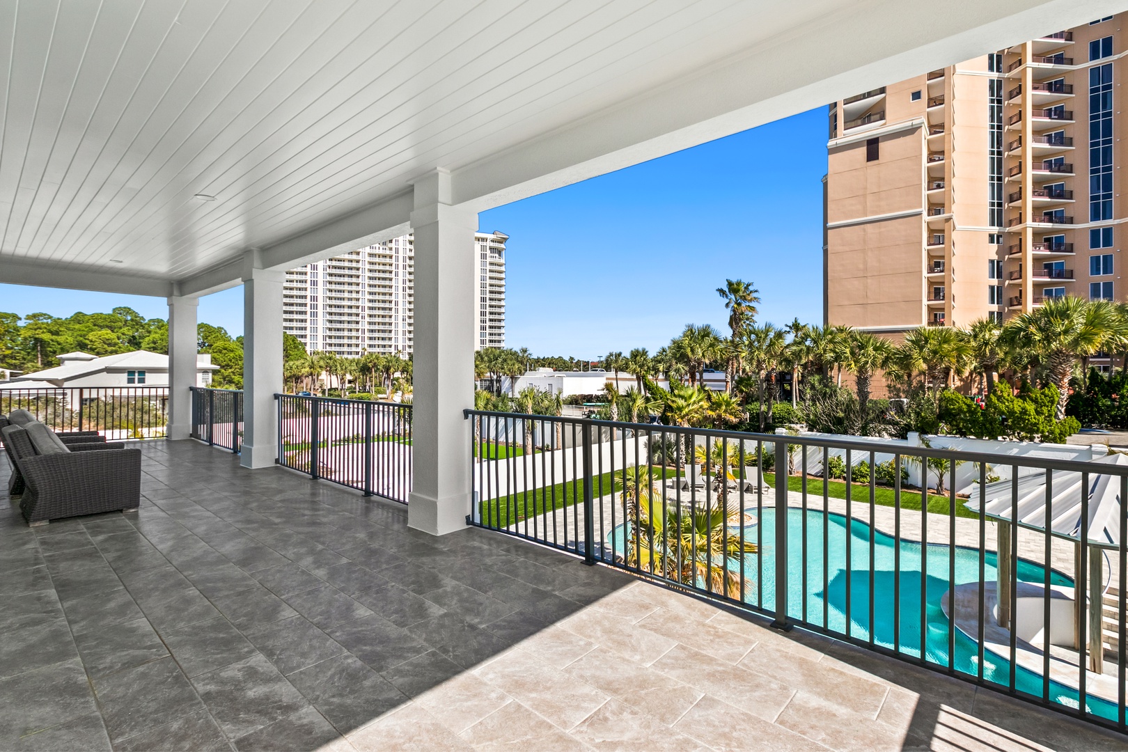 Your private covered balcony overlooks lush tropical palms and the sparkling pool below, with spacious tile flooring perfect for morning coffee or evening relaxation.