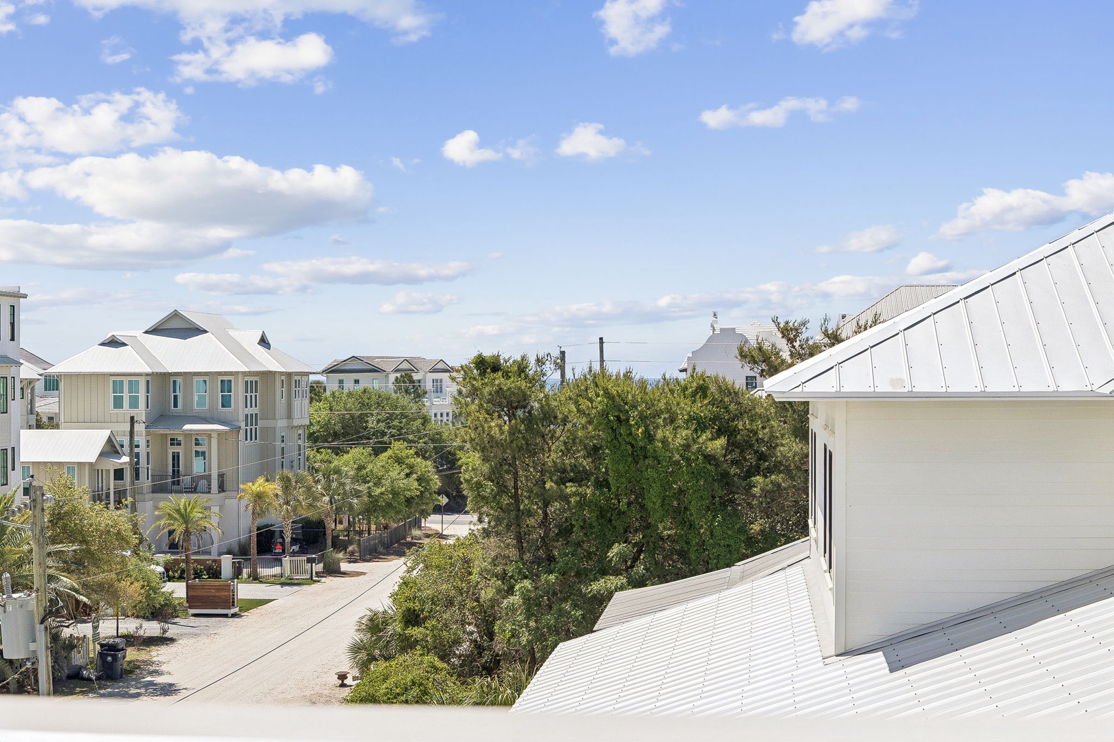 Charming coastal neighborhood surrounds the property with colorful beach houses and tree-lined streets under blue skies.