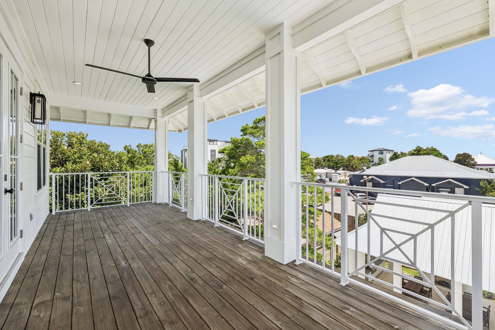 A spacious covered balcony with ceiling fan overlooks a leafy neighborhood, offering a peaceful spot to relax and enjoy the fresh air.