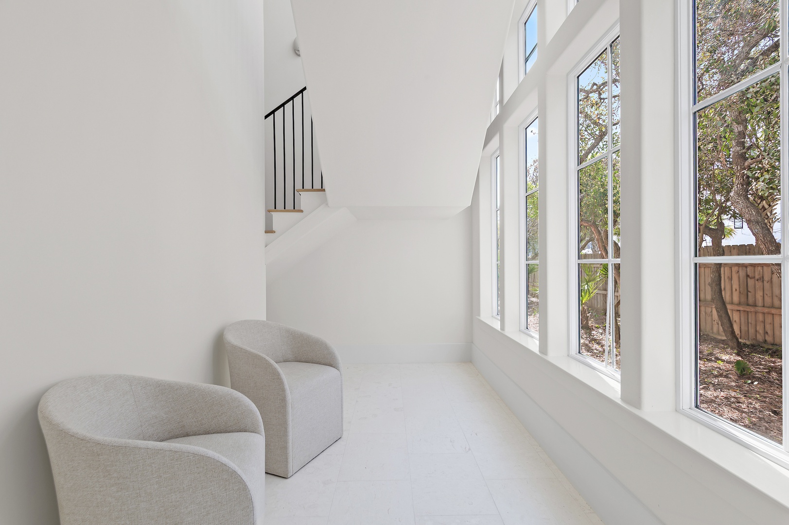Relax in your serene sitting area, where tall windows frame a private backyard view, flooding the space with natural light and a peaceful connection to the outdoors.