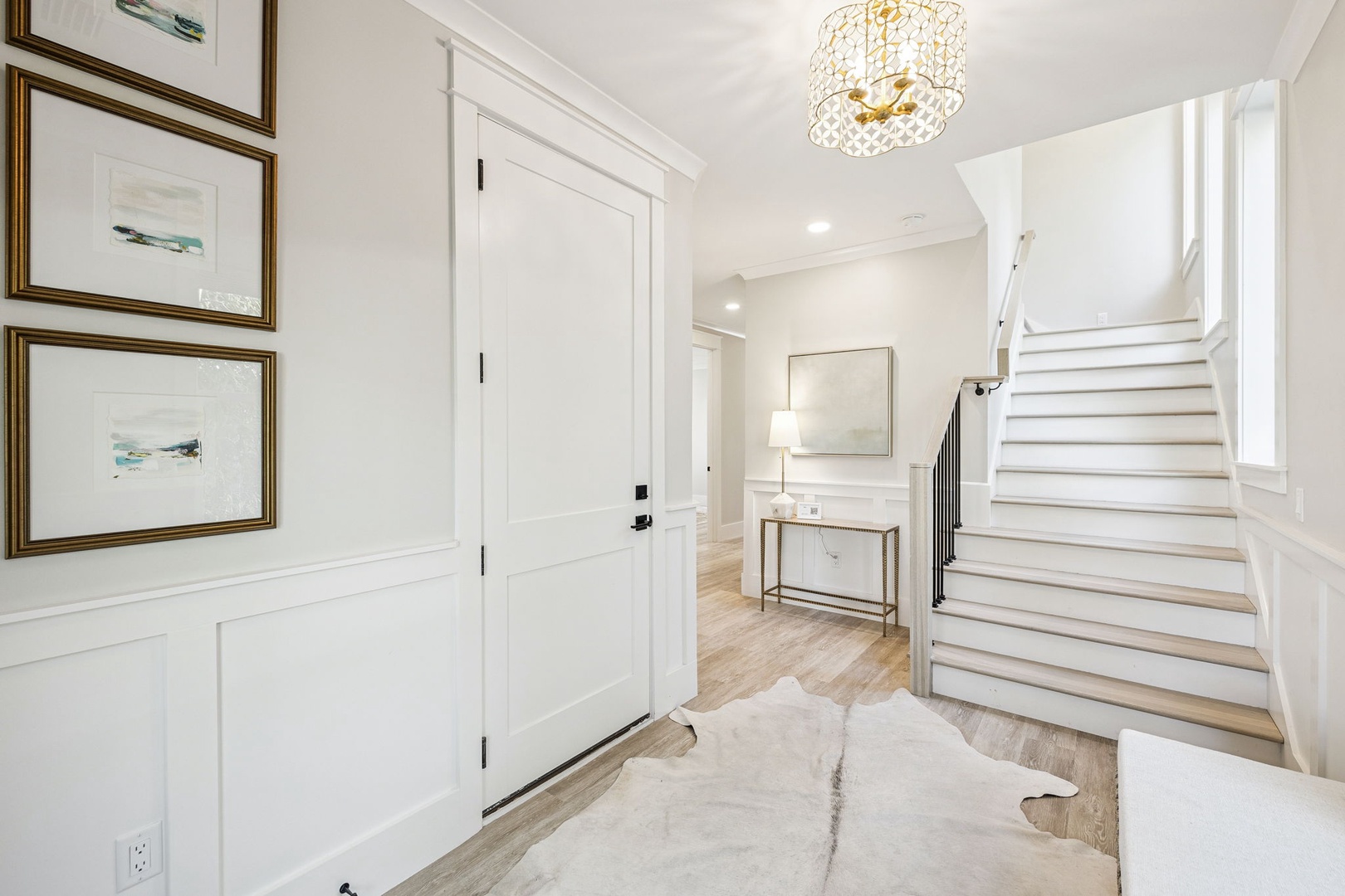 Step into your elegant entryway where coastal artwork and gleaming hardwood floors welcome you home beneath a stunning crystal chandelier.