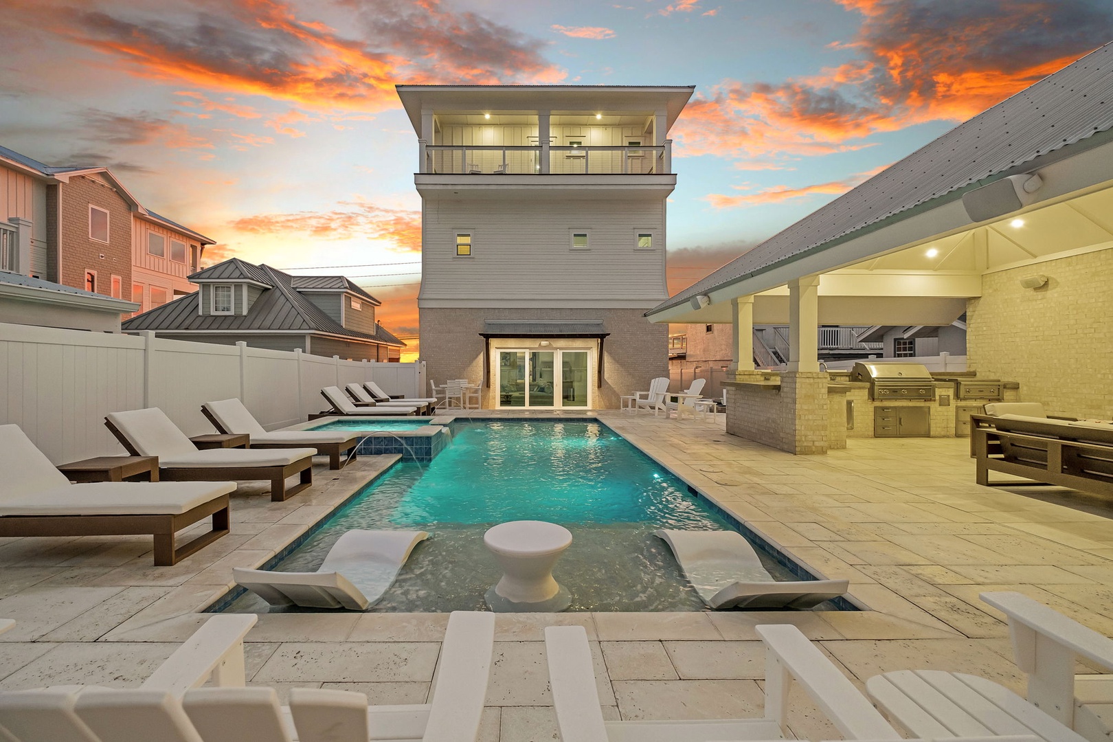 Modern beachside property featuring a luxury pool deck and outdoor kitchen area, captured during a stunning sunset.